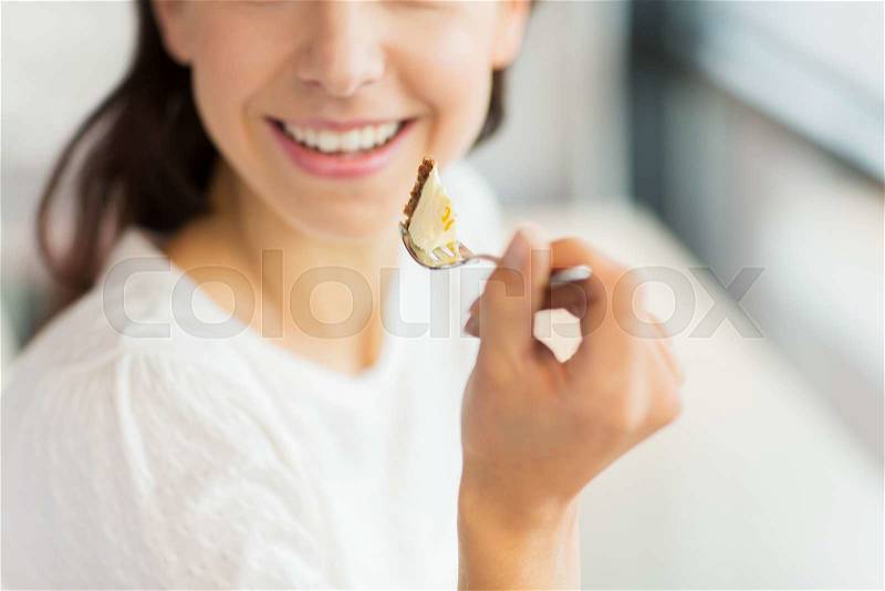 Food, dessert, people and lifestyle concept - close up of smiling young woman holding fork and eating cake at cafe or home, stock photo