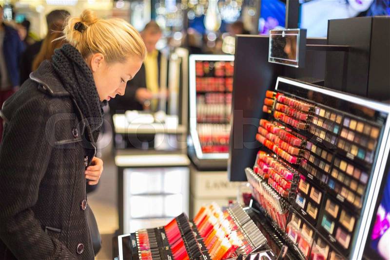 Beautiful blond lady testing and buying cosmetics in a beauty store, stock photo