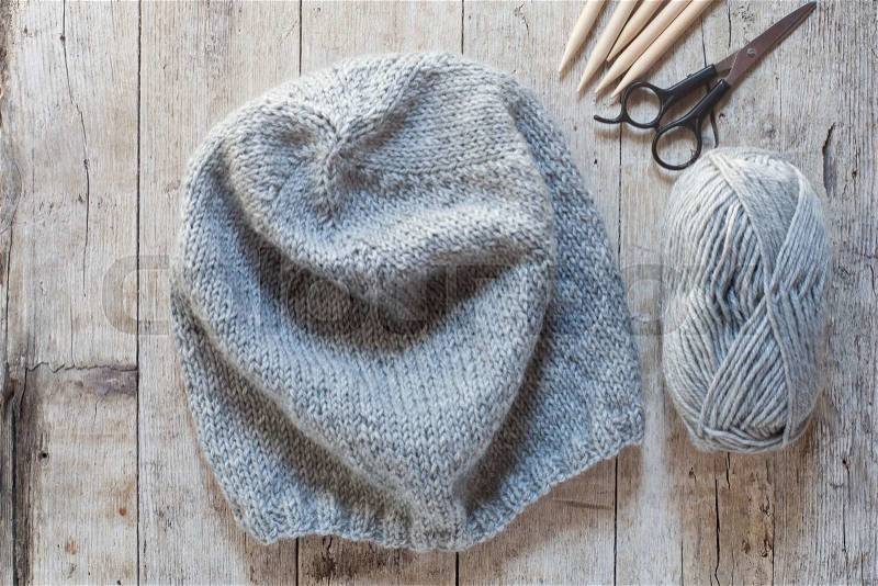 Wool grey hat, knitting needles and yarn on wooden background, stock photo