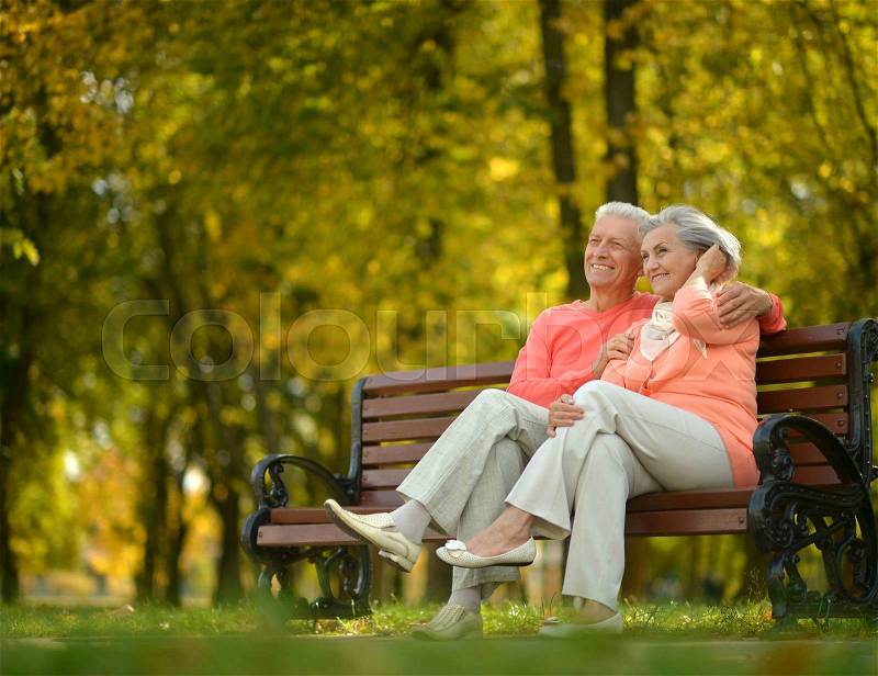Happy elderly couple sitting on bench in autumn park, stock photo