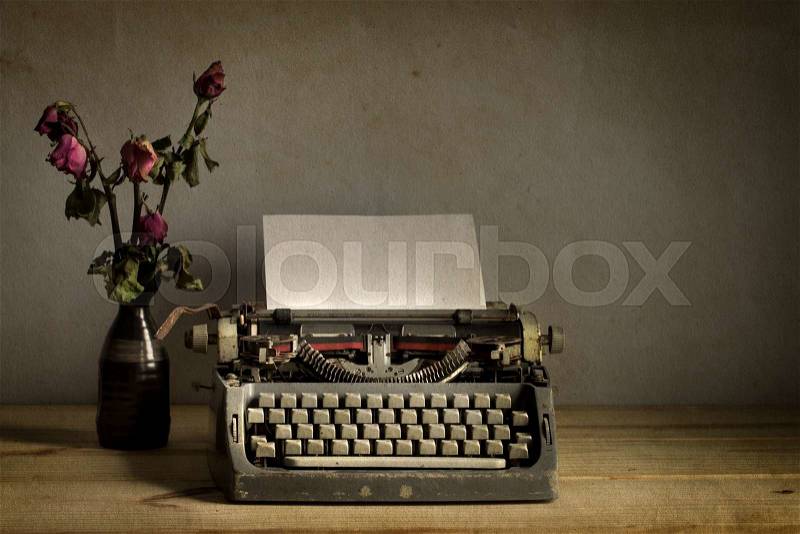 Still life with old typewriter with dry rose flowers on wooden table, stock photo