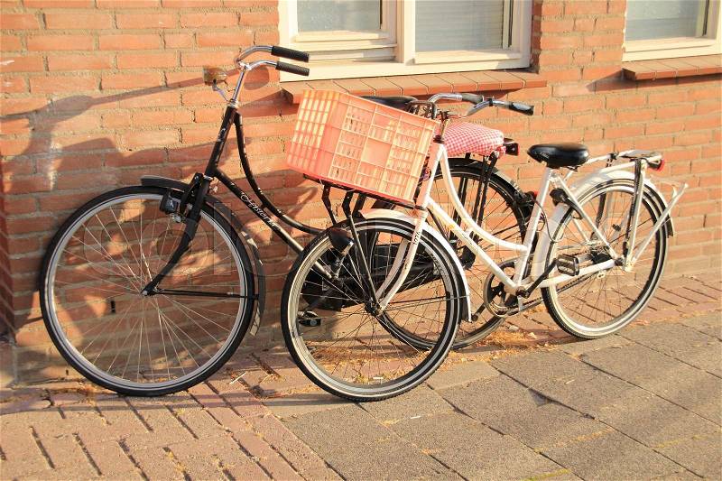 Two bikes, one with pink bicycle basket, stands against the house in the city in the summer, stock photo