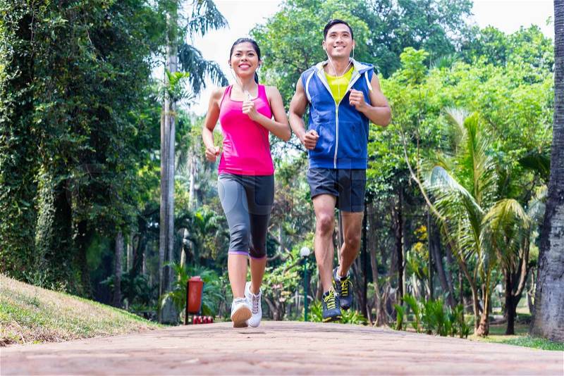 Asian couple, man and woman, jogging or running in tropical Asian park for fitness, stock photo