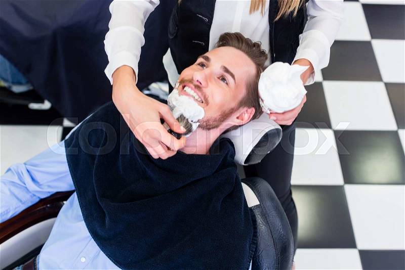 Man getting beard shave in barber salon, stock photo