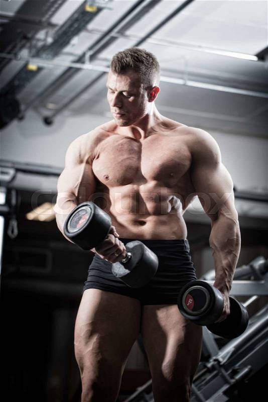 Bodybuilder in gym at fitness training with barbells standing in front of equipment, stock photo