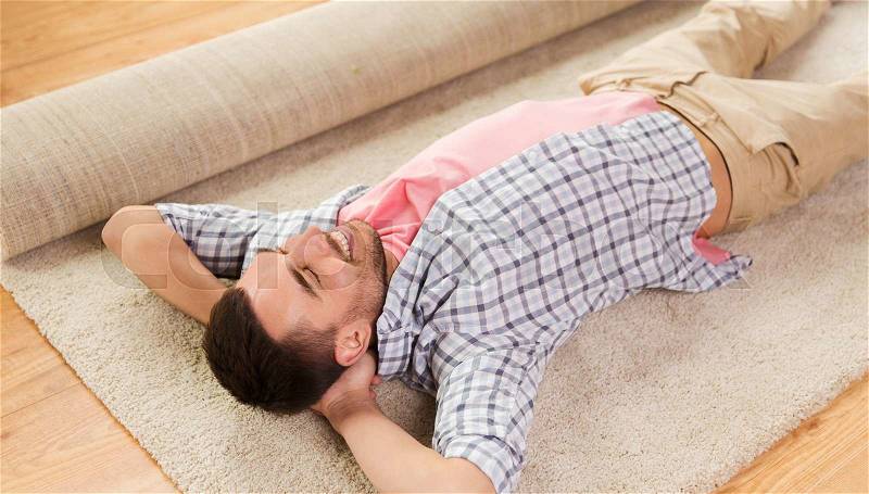 People, repair and renovation concept - happy man lying carpet or rug on floor at home, stock photo