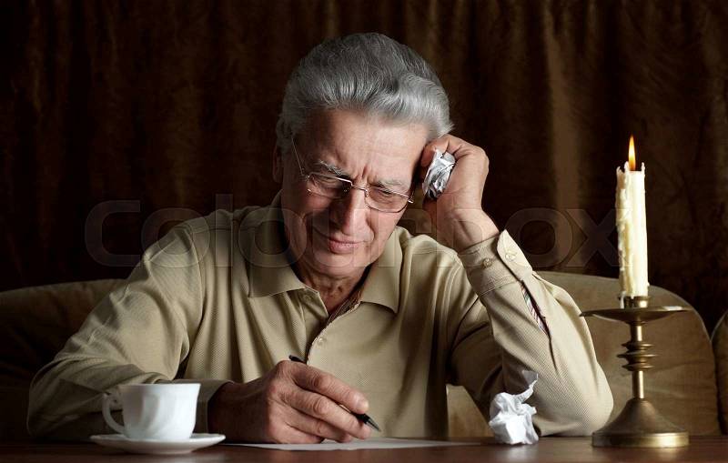 Elderly pensive man writes a letter by candlelight, stock photo