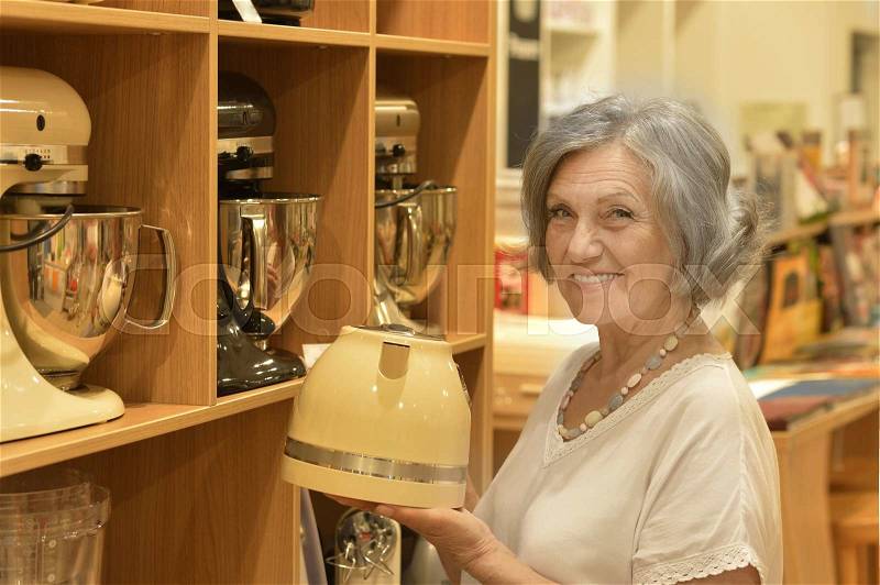 Portrait of old cute smiling lady choosing kettle, stock photo