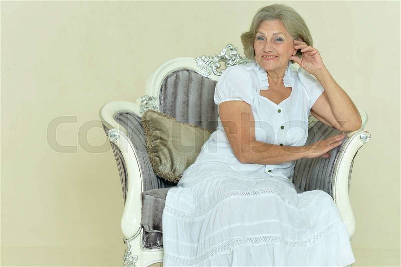 Portrait of beautiful mature woman sitting in vintage chair, stock photo