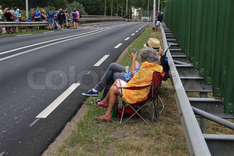 The audience, some sitting or standing, are waiting along the route at the cyclists of the Tour de France in the summer, stock photo