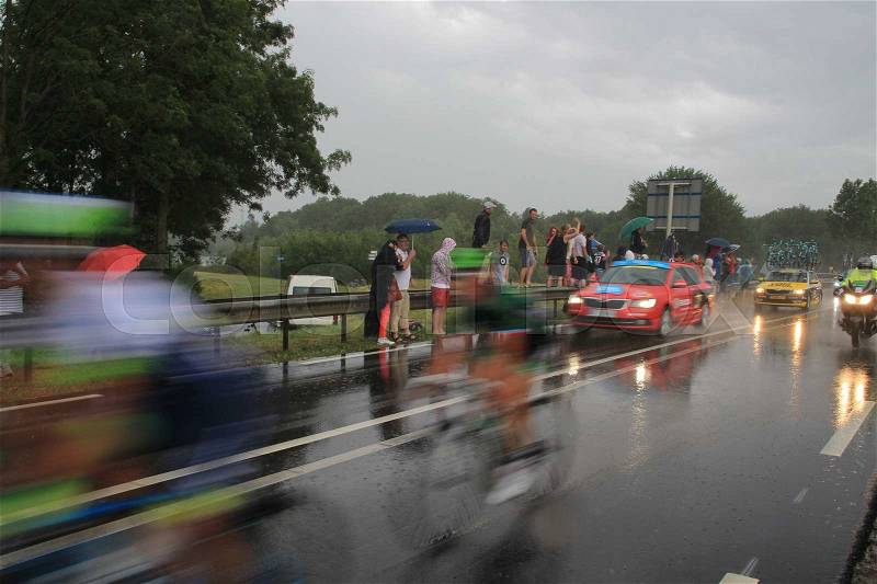 It's raining cats and dogs and the follow cars are driving behind the cyclists of the Tour de France in the bad wheater in the summer, stock photo