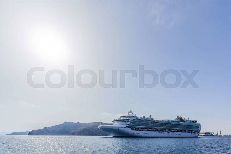 Big cruise liner which is more than a mountain in the background goes from port to travel around the world on a bright sunny day. In the picture: sun, blue sea, a big white ship, stock photo