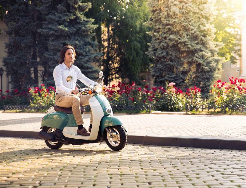 Handsome young man driving scooter in the city park, stock photo