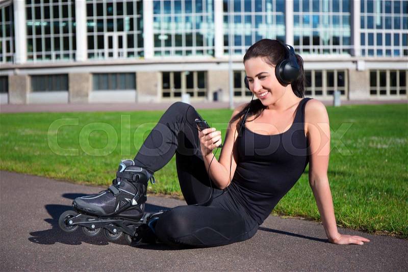Happy woman in roller skates sitting and listening music in summer park, stock photo