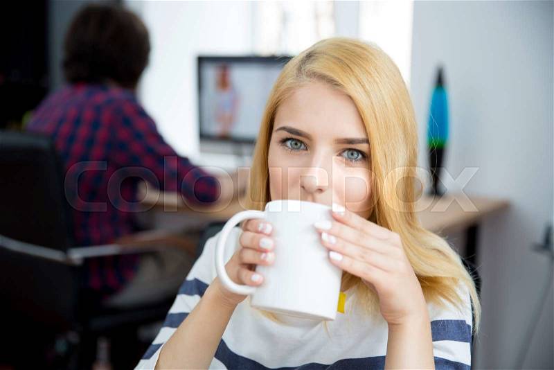 Young casual woman drinking coffee in office, stock photo