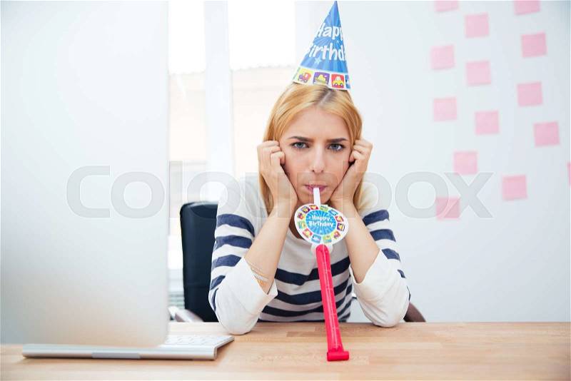 Young girl sitting at the table with party hat in office and blows whistle, stock photo