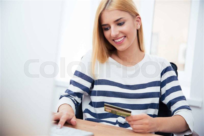 Young casual businesswoman holding bank card and typing on keyboard in office, stock photo
