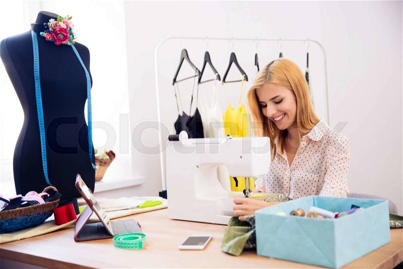 Happy young woman using a sewing machine in laundry, stock photo