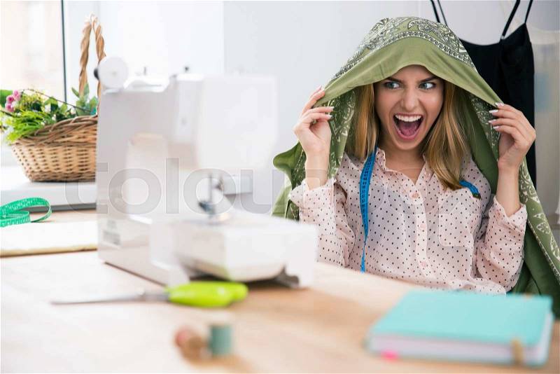 Funny female deisgner sitting at her workplace and screaming, stock photo
