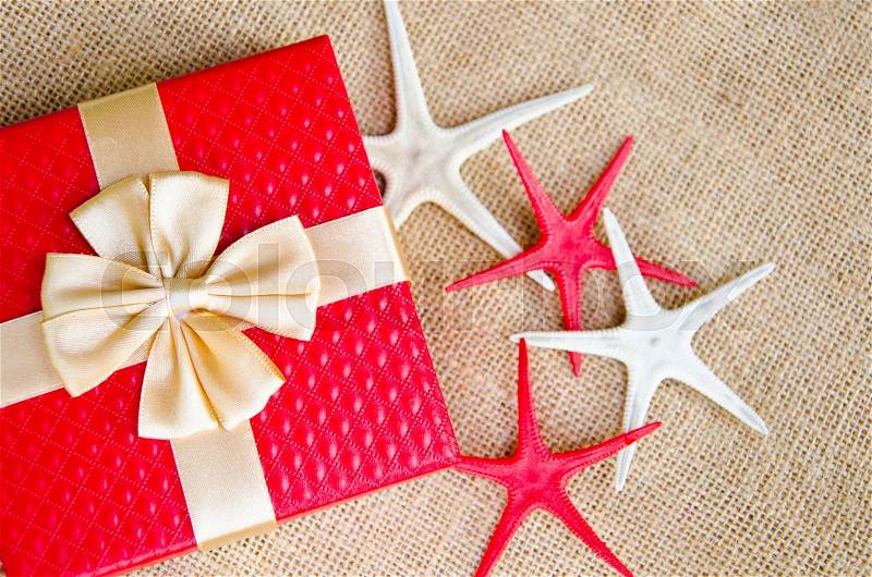 Red gift box with gold ribbon and star fish on sack background, stock photo