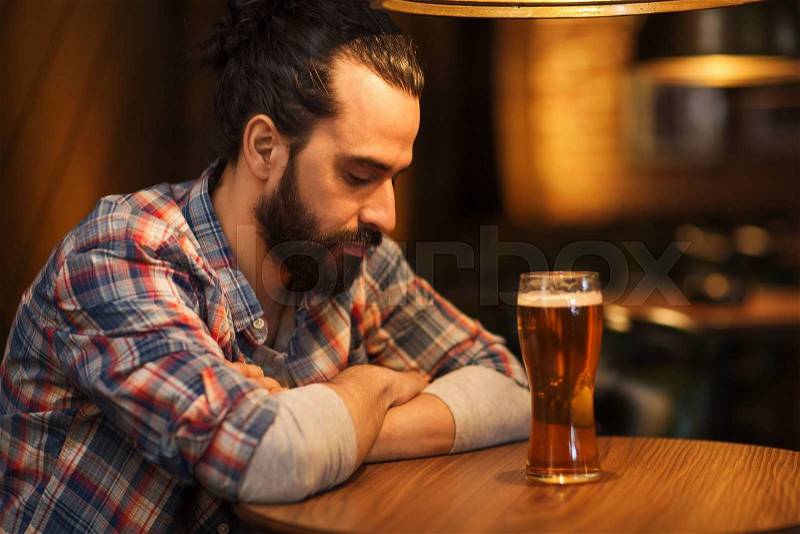 People, loneliness, alcohol and lifestyle concept - unhappy single man with beard drinking beer at bar or pub, stock photo