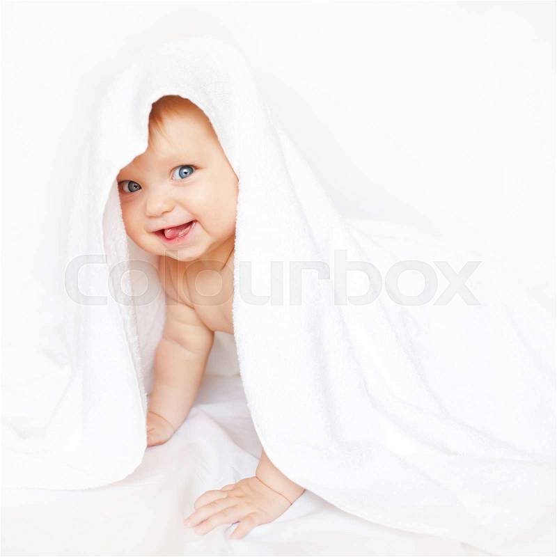 Baby playing hide and seek under the towel and showing tongue, stock photo