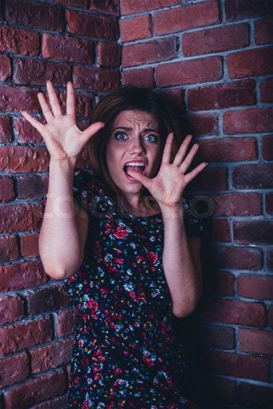 Frightened young woman standing in corner of brick wall, stock photo