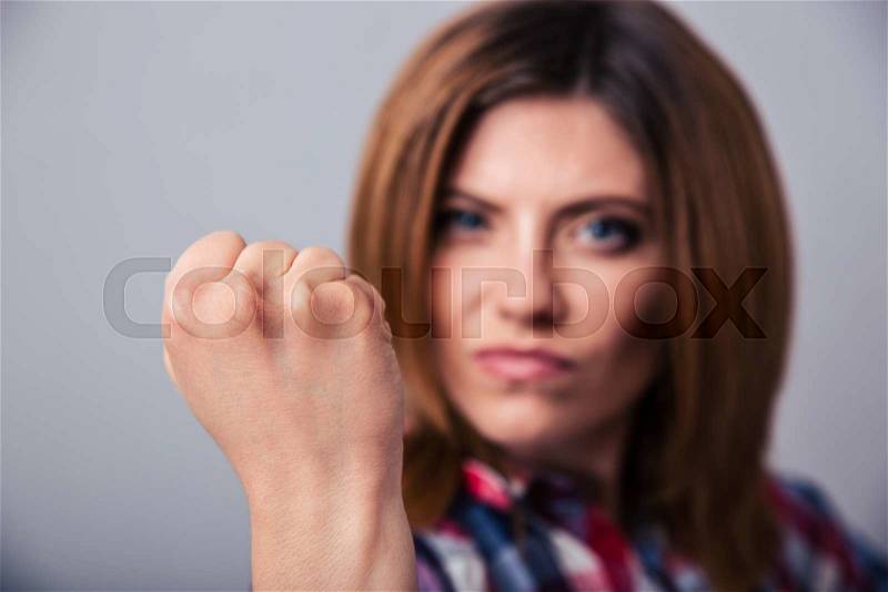 Angry young woman showing fist over gray background. Focus on fist, stock photo