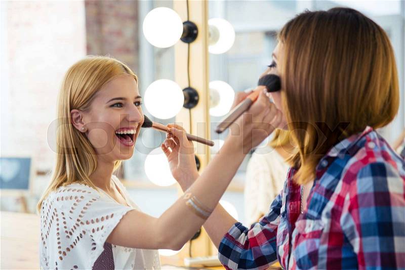 Two happy girlfriends doing makeup to each other, stock photo
