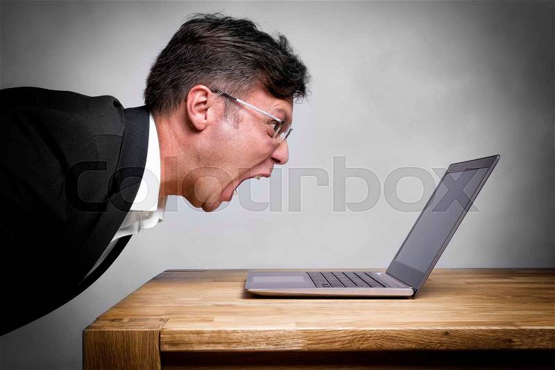 Man sitting at the table and screaming at his laptop, stock photo