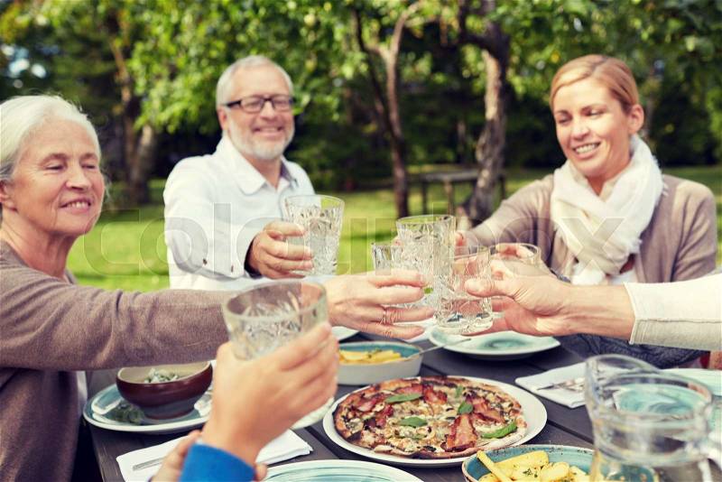 Family, generation, home, holidays and people concept - happy family having dinner and clinking glasses in summer garden, stock photo