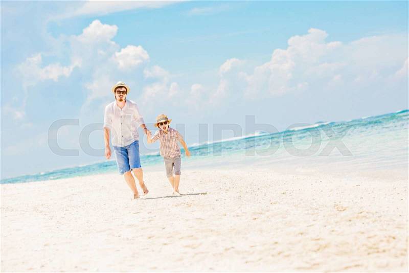 Father and son in summer nats and sunglasses running barefoot on the sea surf line having great holidays time on beautiful sunny day. Bali, Pandawa beach , stock photo
