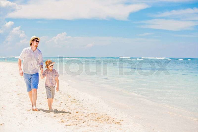 Happy hipster father and his small son having great quality family time enjoying white sand and the ocean on beautiful sunny day on summer holidays, stock photo