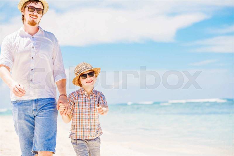Happy hipster father and his small son having great quality family time enjoying white sand and the ocean on beautiful sunny day on summer holidays, stock photo