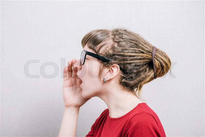 Woman in glasses calling with a hand to her mouth, profile. On a gray background, stock photo