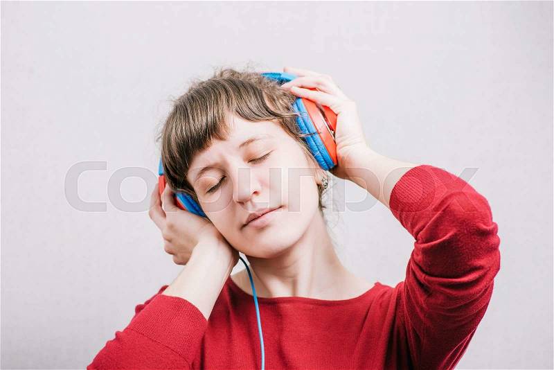 Woman listening to music with his eyes closed. On a gray background, stock photo