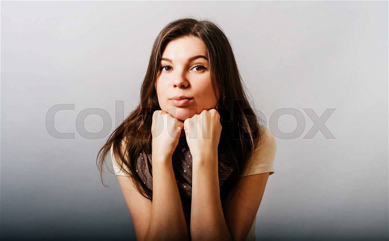 A young woman thinks with his head on two fists. On a gray background, stock photo