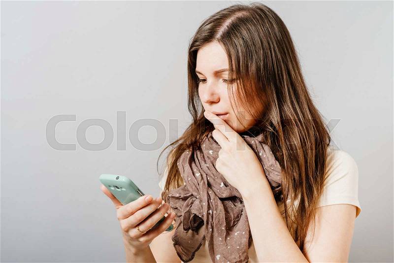 Young woman reading the sad news on the phone. On a gray background, stock photo