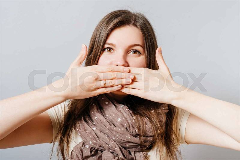 Young woman covering her mouth with her hands. On a gray background, stock photo