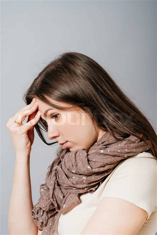Young sad woman lowered her head and put her hand on her profile. On a gray background, stock photo