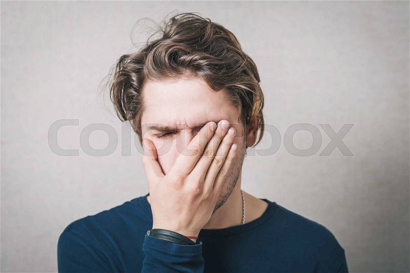 The man was crying, very upset, he covered his face with his hands. Gray background, stock photo
