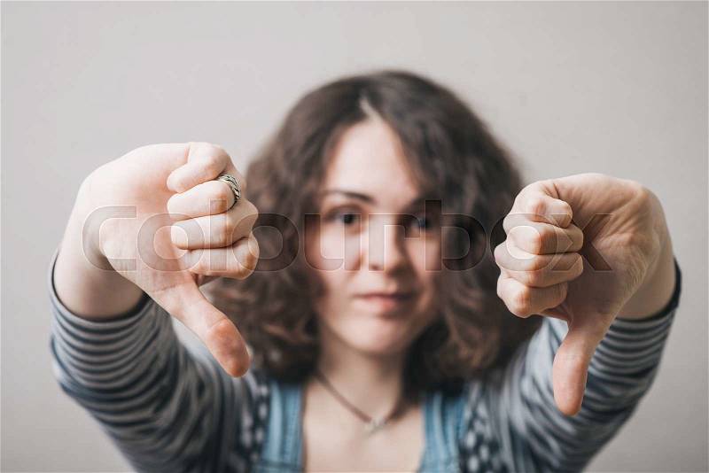 Woman showing two thumbs down. On a gray background, stock photo