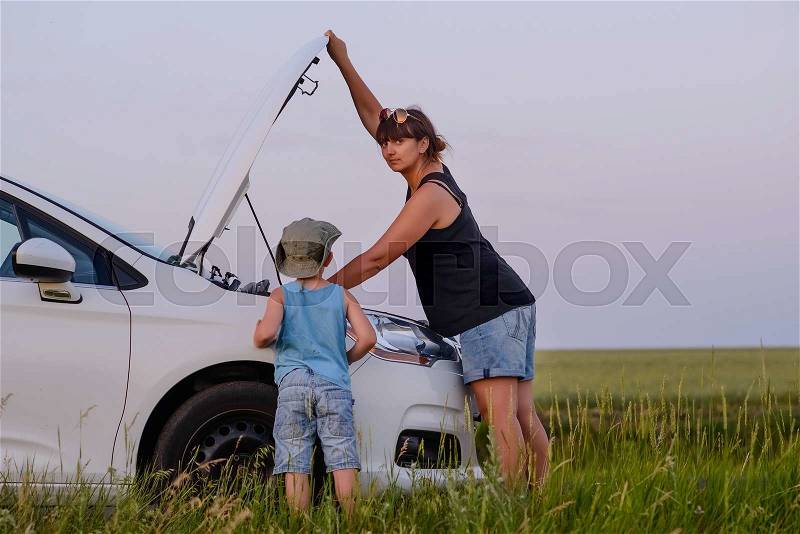 Mom with Son Looking at the Camera While Opening the Front of a Defective Car at the Grassy Ground, stock photo