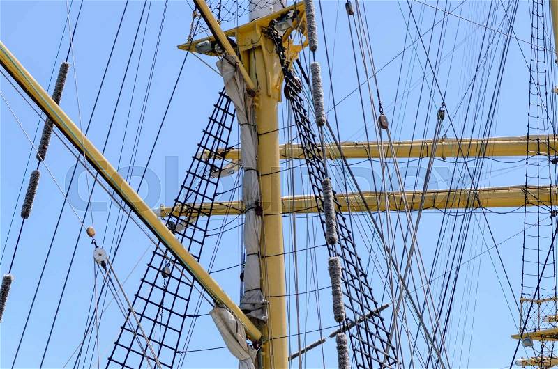 Sailors on the rigging of a tall ship balanced along the yard arm attending to the sails, multiple masts and crew against a blue sky, stock photo