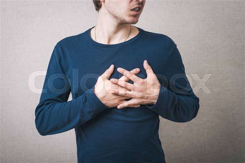 Man hurt heart, hands on his chest. Gray background, stock photo
