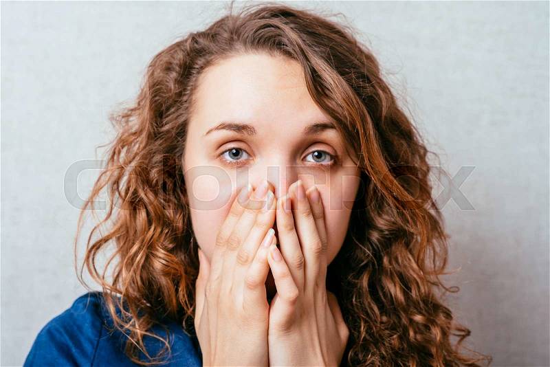 Curly woman coughs, covering her mouth with his hands. Gray background, stock photo