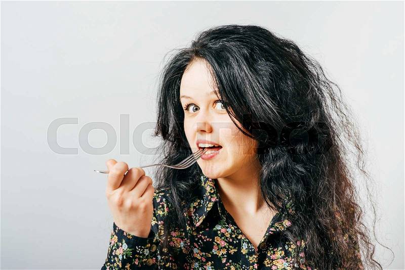 Portrait of young smiling woman with fork in her mouth and (pleasure from eating), stock photo