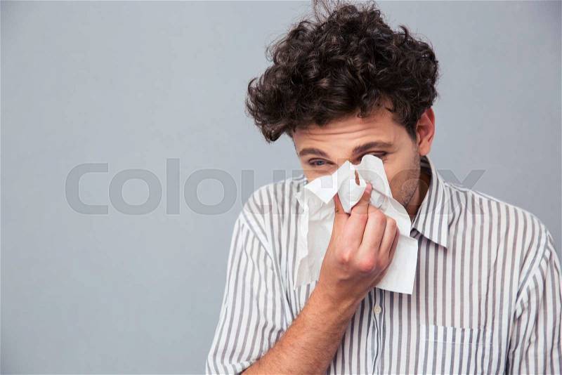 Portrait of a man blowing his nose over gray background, stock photo