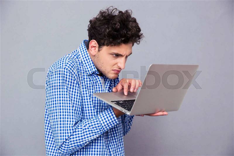 Angry man standing and using laptop over gray background, stock photo