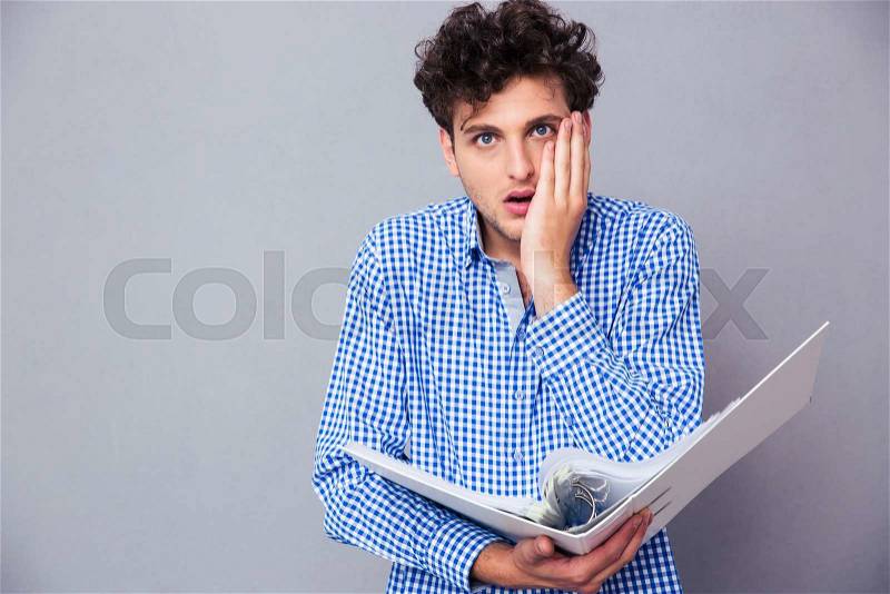 Shocked young man standing with folder of documents and looking at camera, stock photo